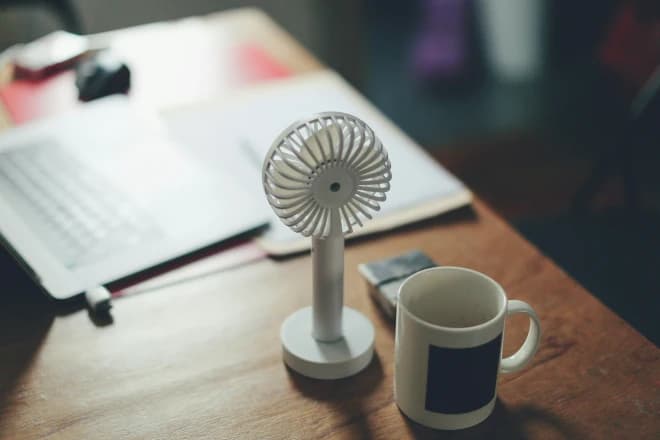 tafelventilator naast een laptop en een koffiemok - symbool voor de menopauze bij ME